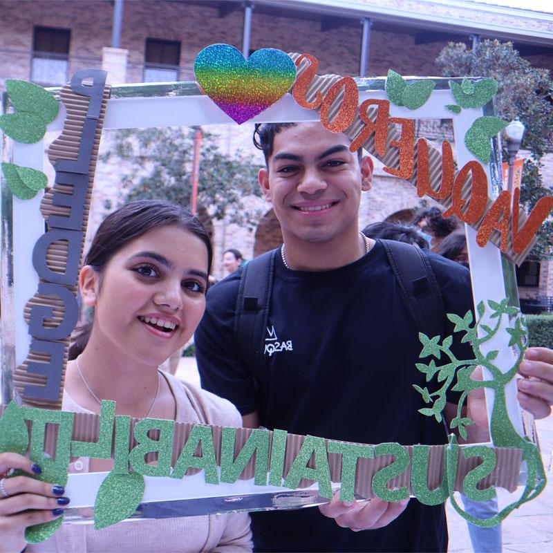 Two students on the Brownsville Campus taking a photo with the Sustainability Pledge selfie frame during Campus Sustainability Day hosted by the Office for Sustainability