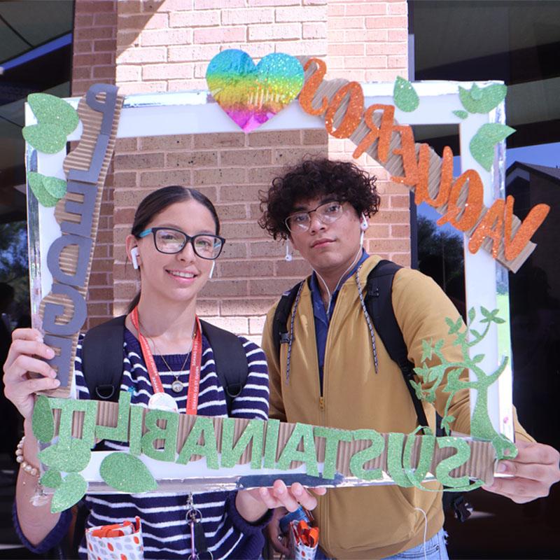 Two students on the Edinburg Campus taking a photo with the Sustainability Pledge selfie frame during Campus Sustainability Day hosted by the Office for Sustainability