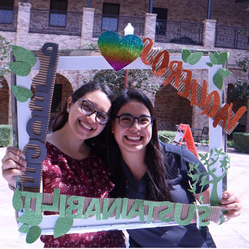 Two students on the Brownsville Campus taking a photo with the Sustainability Pledge selfie frame during Campus Sustainability Day hosted by the Office for Sustainability